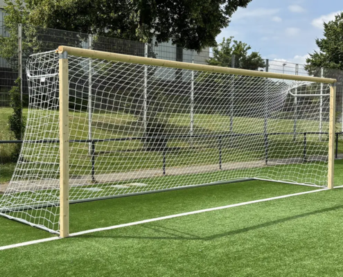 Fußballtor aus Holz mit Aluminiumverbindern, weißem Tornetz und Aluminiumbodenhülsen auf dem Kunstrasen eines Sportplatzes.